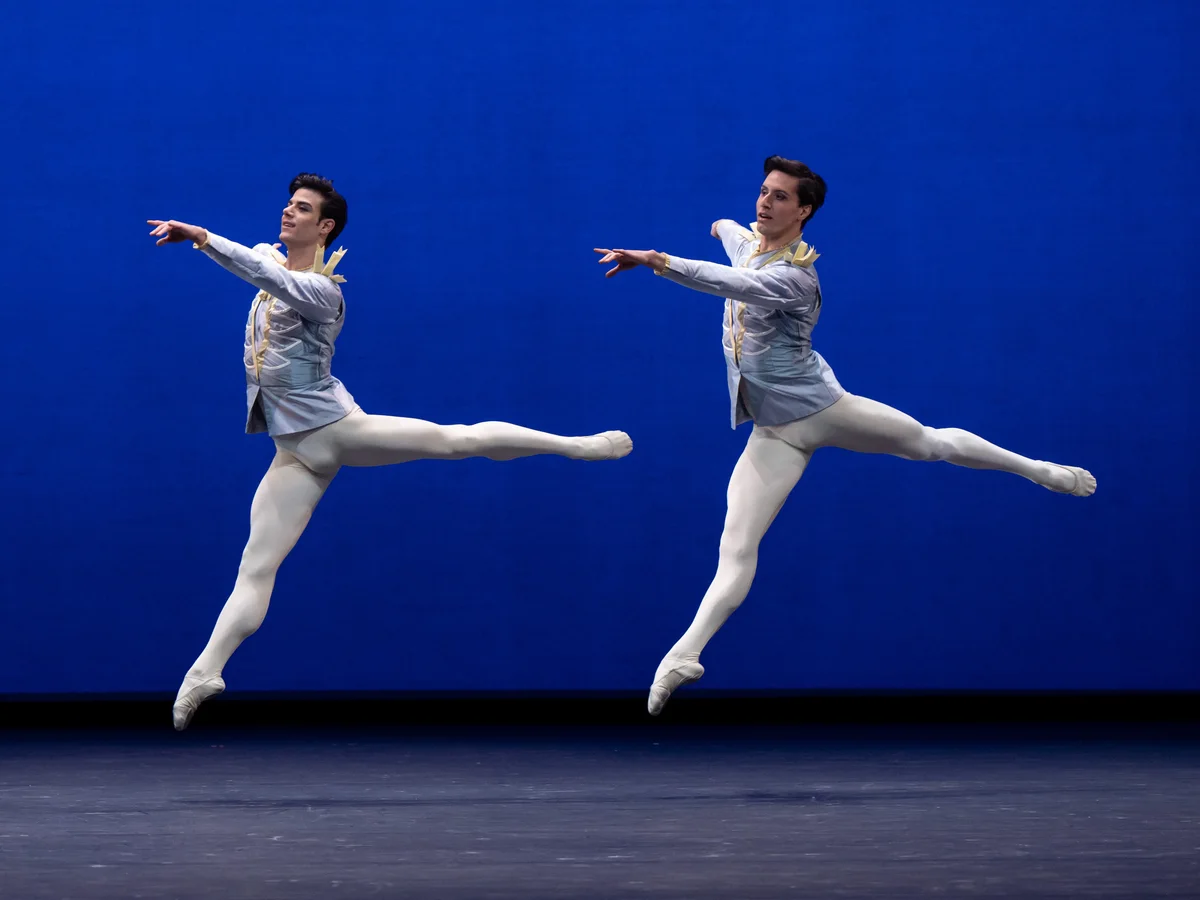Two dancers in pale blue and gold costumes leap in George Balanchine’s Divertimento No. 15.